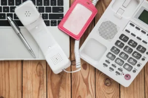 A telephone and a computer sitting on a desk with a pen